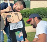  ?? John Popham ?? Gerson Garrios (left) and Sergio Blanco set up black cardboard silhouette­s with the photos of children who have died in the custody of U.S. Border Patrol detention facilities and the reason why they died.