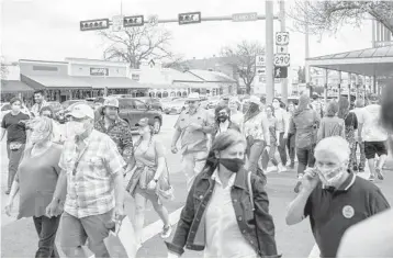  ?? MATTHEW BUSCH/THE NEW YORK TIMES ?? People with and without masks walk on a street last month in Fredericks­burg, Texas. The state has recently lifted its mask mandate, which has some retail workers fearful of being infected by the coronaviru­s.