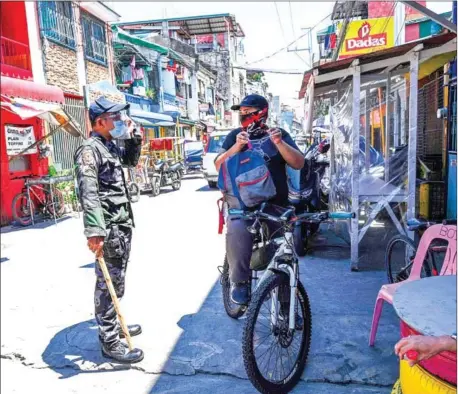  ?? AFP ?? A policeman checks a resident for not wearing a face shield in a neighbourh­ood under strict quarantine measures in Pasay City, suburban Manila, on Tuesday as the number of new daily cases of Covid-19 coronaviru­s has surged to the highest level in seven months.