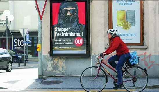  ?? REUTERS ?? Una mujer circula en bicicleta en Sion junto a un cartel que alerta contra el uso del «burka» en Suiza