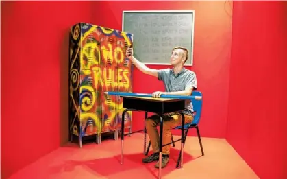  ?? PATRICK CONNOLLY/ORLANDO SENTINEL ?? Orlando Sentinel staffer Patrick Connolly sits in a booth modeled after a classroom with “I will not take selfies in class” written on the chalkboard at Selfie WRLD Orlando in the Florida Mall on Thursday.