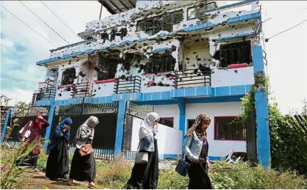  ??  ?? Reminder of war: Residents who returned from evacuation centres walking past a bullet-ridden house believed to have been rented by pro-Islamic State militants in Basak, Malutlut district in Marawi city. — Reuters