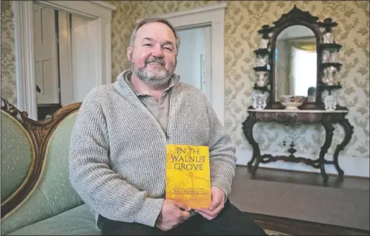  ?? (St. Louis Post-Dispatch/Cheyenne Boone) ?? Florissant Valley Historical Society’s Treasurer Andrew Theising poses for a portrait in the Taille de Noyer with a book he wrote titled “In the Walnut Grove,” which features essays and research about Black history and enslaved people in Florissant, Mo., and other parts of north St. Louis County.