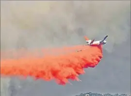  ??  ?? A TANKER PLANE drops fire retardant near California 180. Crews have begun burnout operations to minimize the risk that the fire will jump the road.