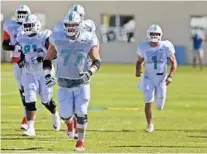  ?? CARL JUSTE/AP ?? Jesse Davis, center, leads fellow Dolphins linemen during a stretching exercise during the early days of training camp on July 28.