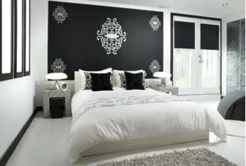  ?? BRANDON BARRÉ PHOTOS ?? White floors and walls with a feature wall in matt black are accented with hound’s tooth end tables and simple throw rugs and white linen. The room is a vision of monochrome elegance.
