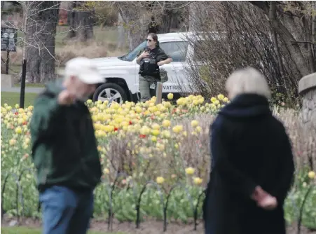  ??  ?? A conservati­on officer keeps an eye on park space in Ottawa as people walk through on Wednesday. Ontario extended emergency measures prohibitin­g the use of parks until May 19 in an effort to contain the spread of COVID-19.
