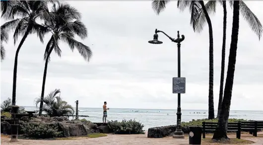  ?? CALEB JONES/AP ?? A man looks out at surfers on Waikiki Beach in Honolulu. People who travel to Hawaii face a two-week quarantine.