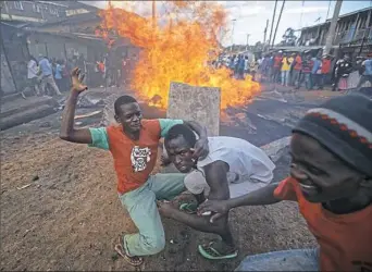  ?? Ben Curtis/Associated Press ?? Opposition supporters crouch behind a piece of metal being used as a heat shield next to a burning barricade during clashes with police Friday in the Kawangware slum of Nairobi,