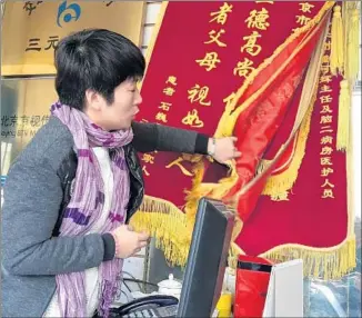  ?? Julie Makinen
Los Angeles Times ?? IN HER BEIJING SHOP, World Brilliant Craft, Zheng Haiyan looks through some jinqi banners, which are coming back into vogue amid the government’s massive anti-graft campaign.