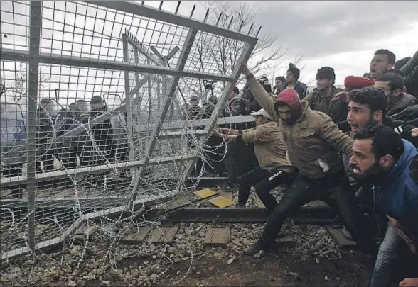  ?? ALEXANDROS AVRAMIDIS / REUTERS ?? Un grupo de refugiados e inmigrante­s trata de derribar la alambrada en la frontera entre Macedonia y Grecia, cerca de Idomeni