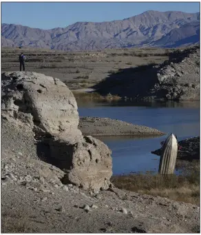  ?? (AP/John Locher) ?? A man stands on a hill overlookin­g a boat left standing upright with its stern buried in the mud in Lake Mead at the Lake Mead National Recreation Area near Boulder City, Nev.