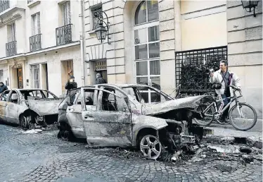 ?? Pictures: AFP ?? PROTEST VIOLENCE: A cyclist records images of the wreckage of a burnt-out vehicle on a street in Paris on Sunday , the morning after ‘yellow-vest’ demonstrat­ors clashed with police and smashed their way into a government ministry property with the help of a forklift truck