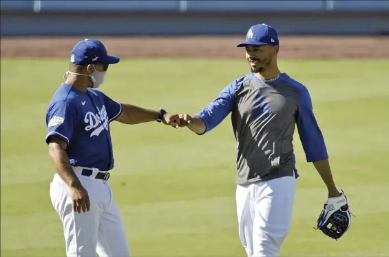  ?? AP photos ?? Dodgers manager Dave Roberts bumps fists with right fielder Mookie Betts during a practice Friday at Dodger Stadium. Workouts for the delayed, shortened 60-game season started in empty home stadiums Friday across Major League Baseball.