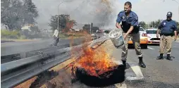  ?? /PHOTOS/ SANDILE NDLOVU ?? A police officer extinguish­es fire from a burning tyre during protests in Soweto yesterday.