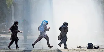  ??  ?? • En Viena, mujeres corren a través del chorro en la plaza Praterster­n para refrescars­e.