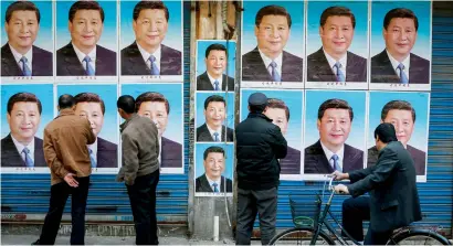  ?? AP ?? People stop and take a close look at a building covered in posters of President Xi Jinping in Shanghai. —