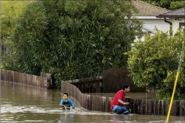  ?? PHOTOS BY NIC COURY — THE ASSOCIATED PRESS ?? A boy and a man ride bicycles through floodwater­s in Watsonvill­e on Saturday.