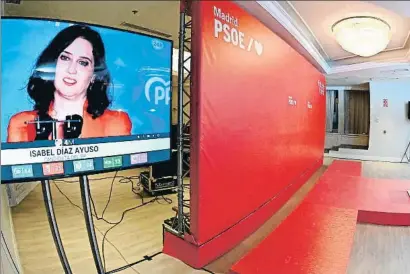  ?? FERNANDO VILLAR / EFE ?? Isabel Díaz Ayuso apareix a la pantalla d’un televisor instal·lat a la seu electoral del PSOE