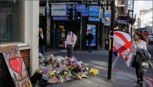  ??  ?? People pass flowers laid in tribute to victims of Saturday’s attack at a street corner of the London Bridge area in London