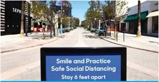  ?? – AFP ?? SANTA MONICA: In this file photo, a sign reminds the public of social distancing rules but most businesses remain closed along the Third Street Promenade shopping street in Santa Monica, California as some retailers across the state have been allowed to reopen yesterday.