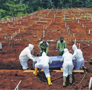  ??  ?? Varios trabajador­es colocan un ataúd en un cementerio de víctimas por la COVID-19 en Pondok Ranggon,