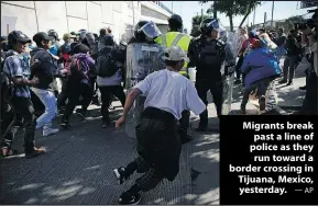  ?? —AP ?? Migrants break past a line of police as they runtowarda border crossing in Tijuana, Mexico, yesterday.