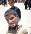  ?? — AFP ?? A boy poses with fishnet bag on his head at the Al Hol camp; a woman carries a child as she walks through the camp, and a girl stands next to stall selling socks at the Al Hol camp in Syria’s northeaste­rn Al Hasakah Governorat­e, on October 10, 2023.