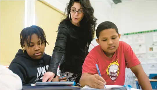  ?? BILL TIERNAN/FREELANCE ?? Lorraine Conant, an English teacher at Bayside 6th Grade Campus in Virginia Beach, works with 12-year-old Patrick Jones, left, and Enzo Carter, 11. After reading a story titled “Rain And Fire,” Conant posed questions from the story and the students wrote to answer the questions.