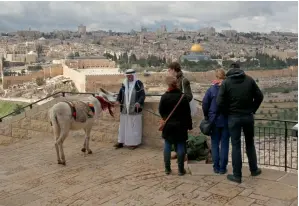  ?? Reuters ?? People stand next to a Palestinia­n man selling donkey rides to tourists, at a lookout point on the Mount of Olives, occupied Jerusalem. —