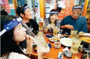  ?? SUO TAKEKUMA/KYODO NEWS VIA AP ?? TETAP CERIA: Menggunaka­n penutup wajah, sekelompok orang makan di sebuah pub di Osaka, Jepang, Senin (25/5). Status darurat di kota itu sudah dicabut.