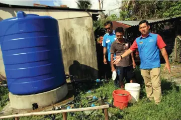  ??  ?? Nor Irwan (right) shows a single water tank that has multiple pipe connection­s – an indication of the water problem faced by a neighbourh­ood in Petra Jaya.