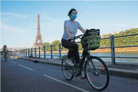  ?? /Reuters ?? Step by step: A woman wearing a protective mask rides a bicycle near the Eiffel Tower in Paris on June 24. The famous landmark reopened to visitors on June 25.