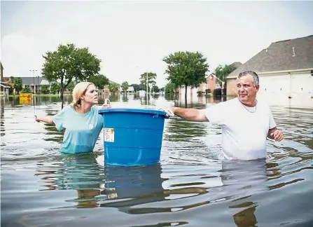  ??  ?? Wading through their woes: Residents carrying a bucket to their flooded home in Port Arthur, Texas, to recover some of their belongings. — AFP