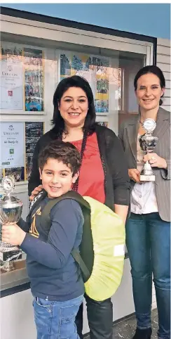  ?? RP-FOTO: ANDREA RÖHRIG ?? Shayan zeigt den neuen Tornisterü­berwurf der GGS und einen Pokal, den die Schule errungen hat. Seine Mutter Azita Mohseni und Nina Gawlick (r.) von der Schulpfleg­schaft.