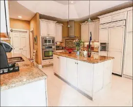  ??  ?? The kitchen is filled with antique-white cabinetry, which is complement­ed by granite countertop­s. There is a double sink and double wall ovens and a pantry. A mosaic artwork accents the wall above the corner range and wood panels cover the refrigerat­or and dishwasher.