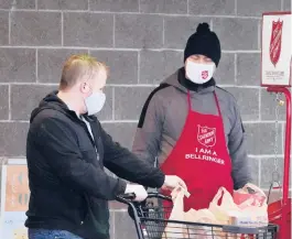  ?? ELAINE THOMPSON/AP ?? A shopper readies a bill to drop in the red collection kettle as Salvation Army bell ringer Michael Cronin, right, looks last week in Linden, Wash. Despite record amounts of donations, nonprofits across the country are being suffocated by the effects of the pandemic.