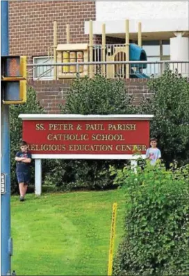  ?? LESLIE KROWCHENKO — DIGITAL FIRST MEDIA ?? Saints Peter and Paul fourth grader Aidan Hughes, left, and parish member Wyatt Morelli, right, stand near the school sign. The pipeline marker is 75 feet from the kindergart­en playground.