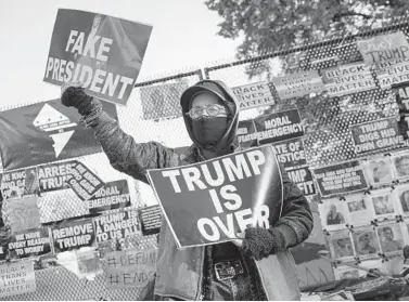  ?? JOHN MINCHILLO/AP ?? A demonstrat­or stands in front of a fence covered in protest signs Nov. 2 on the north side of the White House. Voters went to the polls the following day to choose between giving President Trump a second term in office or replacing him with former Vice President Joe Biden. The Electoral College this week affirmed Biden’s victory and he will be inaugurate­d Jan. 20.