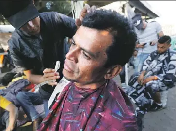  ?? Photograph­s by Luis Sinco Los Angeles Times ?? BARBERS GIVE men haircuts and shaves at Tijuana’s Benito Juarez Sports Center, which has become an emergency migrant camp as thousands of Central Americans arrive after trekking through Mexico.