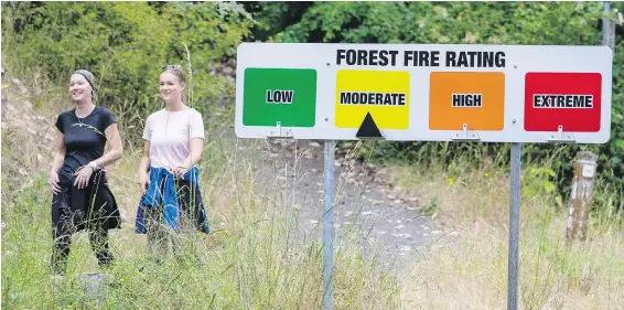  ??  ?? Hikers pass a forest-fire rating sign labelling the risk as moderate in Saanich’s Mount Douglas Park on Thursday. Officials are warning users of all Island parks to be cautious.