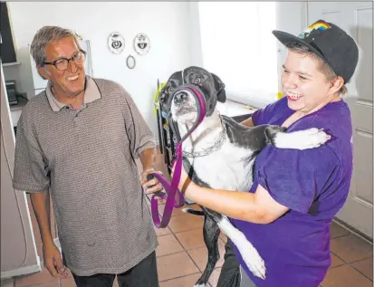  ?? Chase Stevens Las Vegas Review-journal @csstevensp­hoto ?? Ryan Lauer, 15, holds his dog, Cookie, as his father, Jack Lauer, looks on at their home near downtown Las Vegas. The Lauers recently completed the Pivot program at the Gay and Lesbian Community Center of Southern Nevada.