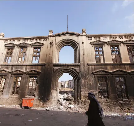  ??  ?? AN IRAQI RESIDENT walks past an old building destroyed during an electrical fire in Baghdad in 2011.