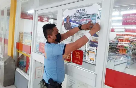  ?? Mabalacat police photo ?? REPORT CRIMES. local police.
A policeman installs a poster with police hotlines as residents are encouraged to report crimes to the