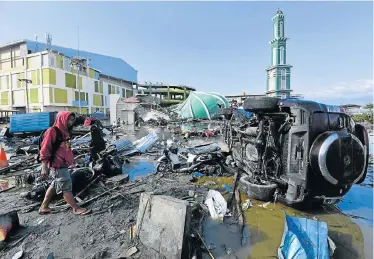  ?? Picture: AFP ?? WIPED OUT: A man walks among vehicles and other wreckage – with a collapsed mosque in the background – in Palu, following the earthquake and tsunami