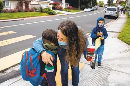  ?? ARIANA DREHSLER ?? Andrea Morales hugs her son Reece while Keiran stands nearby in front of Tierrasant­a Elementary School before dropping them off for their first day of in-person school on Monday. Tens of thousands of local students returned to classrooms.