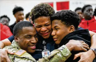  ?? PHOTOS BY JOHN AMIS FOR THE AJC ?? Therrell High School Officer L.J. Williamson hugs her sons, Justin (right) and Army Spec. Shakir Aquil, who surprised her with his return home from a two-year deployment in Korea. Family, friends and staffers secretly orchestrat­ed the mother and son reunion using a pep rally as a ruse.