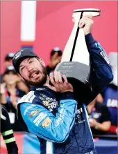  ?? AP PHOTO BY CHUCK BURTON ?? Martin Truex Jr struggles to raise the trophy in Victory Lane after winning a NASCAR Cup Series auto race at Charlotte Motor Speedway in Concord, N.C., Sunday.