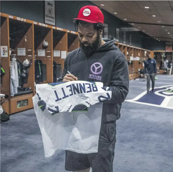  ?? — STEVE RINGMAN /THE SEATTLE TIMES VIA AP ?? Seahawks’ Michael Bennett signs one of his jerseys for another departing player in the Seahawks locker-room on the day after their season ending game on Jan. 1. Bennett knows that being cut is a possibilit­y if not an expectatio­n.