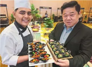  ?? — Photos: cs Nathan/the Star ?? ho (right) with a tray of nasi lemak sushi while Malay cuisine chef arif haqimmi presents appetisers from the club’s buffet dinner.